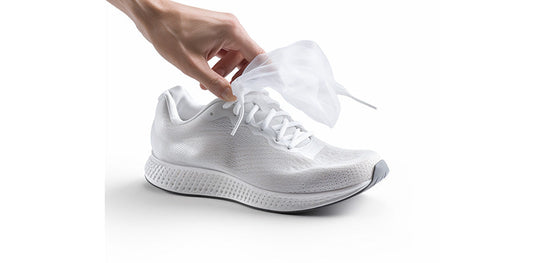 hand with a dryer sheet and a white athletic shoe